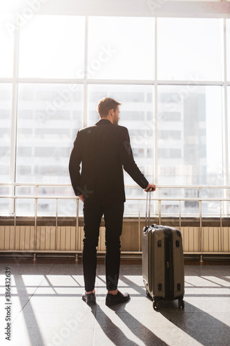 Man standing with a suitcase near the huge window photo