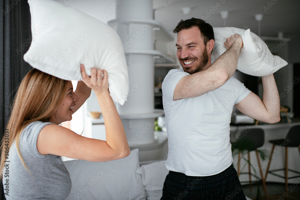 Fototapeta premium Husband and wife fighting pillows on the bed. Young couple having fun at home.