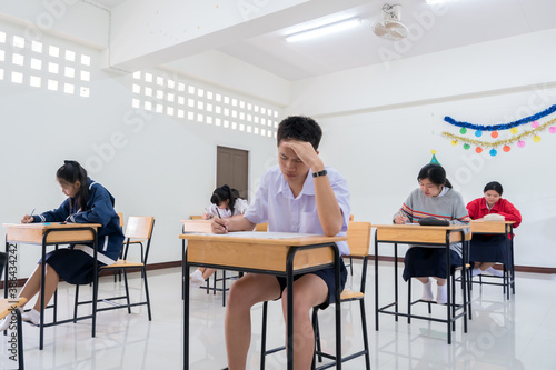 Students Asian undergraduate testing of examination in room sitting serious on row chair doing final exams in classroom with Thailand uniform