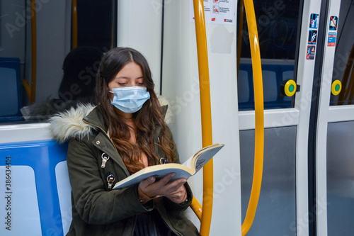 Mujer joven leyendo en el metro con un libro en la mano y con mascarilla