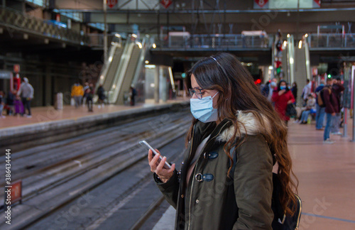  en Mujer revisando el teléfono móvil con mascarilla en una estación de tren en Madrid