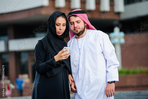 Arabic couple posing outdoors with mob phone in the hands.
