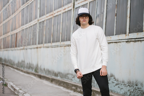 Man wearing white sweatshirt and a black hat standing over gray background. Sweatshirt or hoodie for mock up, logo designs or design prints with with free space. © 4Max