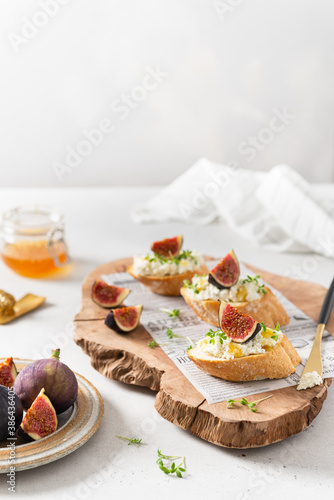 Sandwiches with ricotta cheese, figs, honey and microgreen on wooden board on white background. Side view, copy space. Italian Bruschetta Menu, recipe