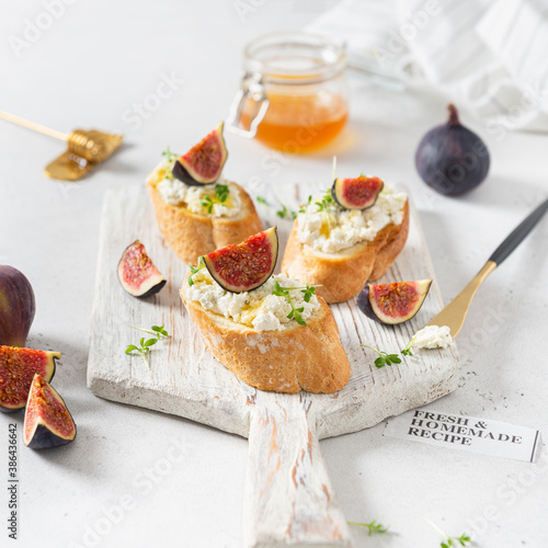 Sandwiches with ricotta cheese, figs, honey and microgreen on wooden board on white background. Side view, close up. Italian Bruschetta Menu, recipe, square