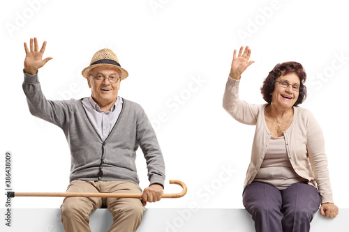 Elderly man and woman sitting on a blank billboard sign and waving at the camera
