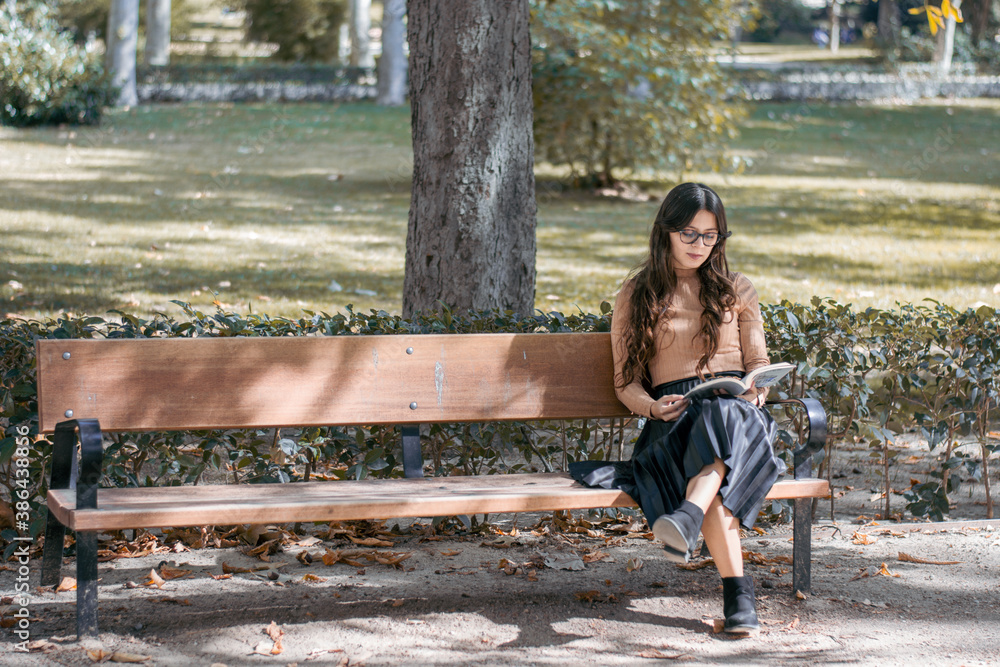 Mujer joven con un libro en la mano en un paisaje de otoño y sentada en un banco Mujer joven con un libro en la mano en un paisaje de otoño y sentada en un banco