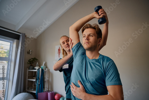 Photography Physiotherapist instructing male patient correct exercise form with dumbbells
