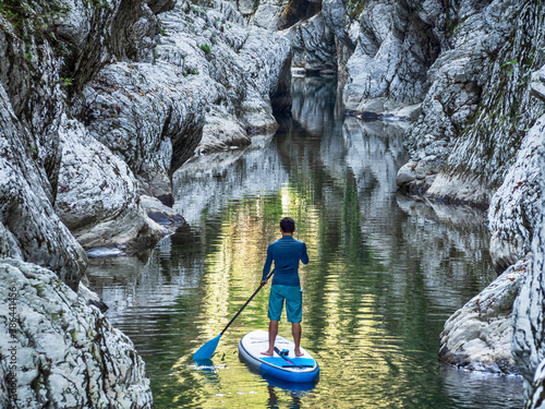 Canvas Print Surfer floating on stand up paddle board on river water in rocky canyon