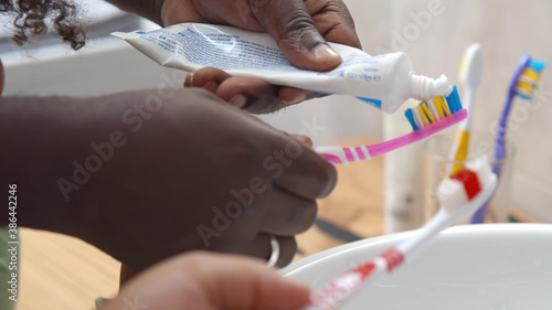 Close up of african kid and parent squeezing toothpaste on toothbrush cleaning teeth in bathroom