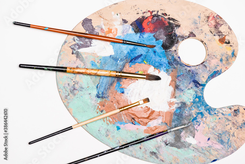 top view of palette with paints and paintbrushes isolated on white