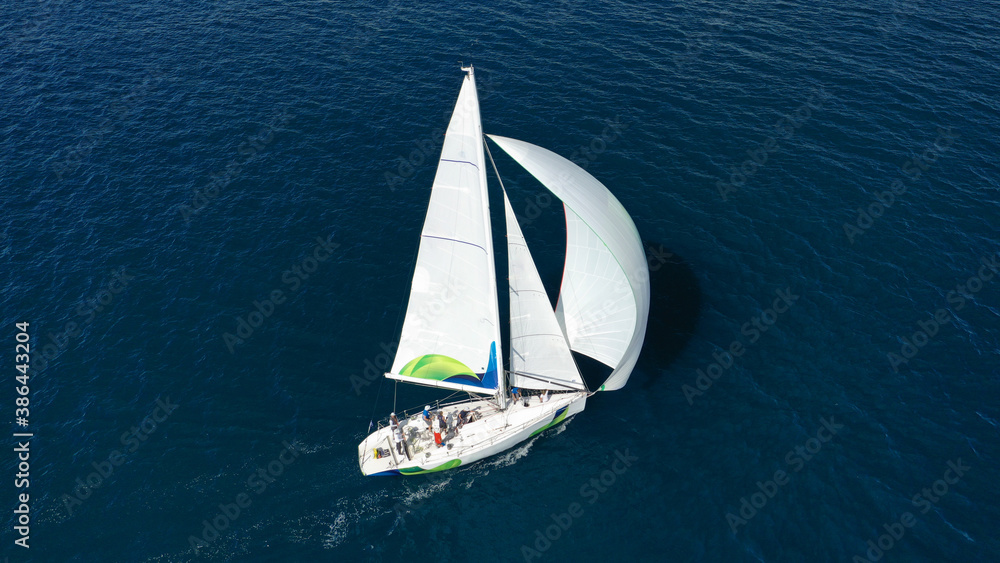 Fototapeta premium Aerial drone photo of beautiful white sailboat with wooden deck cruising in deep blue Aegean sea near Santorini island, Cyclades, Greece