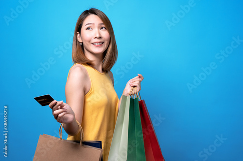 Happy asian beautiful woman holding a shopping bag on it and a credit card, Isolated on a blue background.