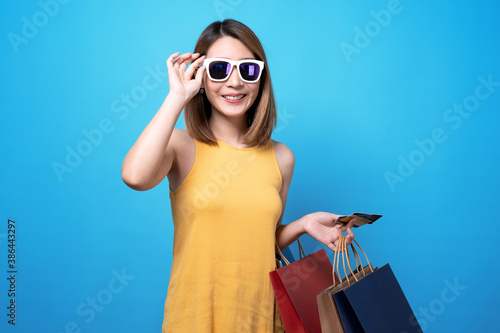 Happy asian beautiful woman holding a shopping bag on it and a credit card, Isolated on a blue background.