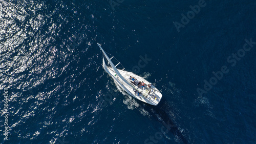 Aerial drone photo of beautiful white sailboat with wooden deck cruising in deep blue Aegean sea near Santorini island, Cyclades, Greece © aerial-drone