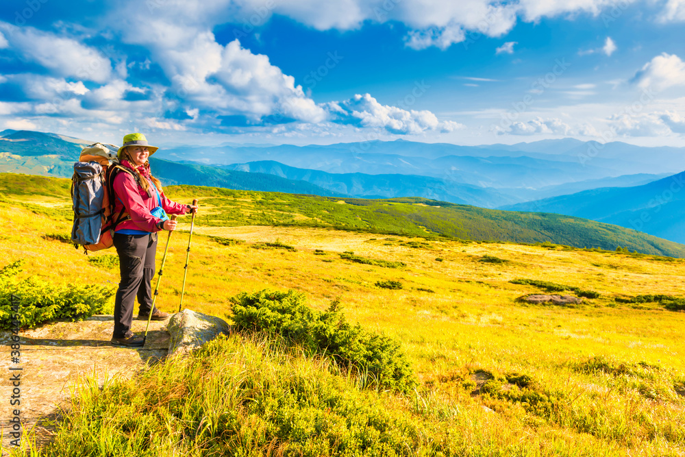 Happy traveling woman with backpack looking at mountain landscape