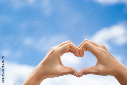 A woman s hand made a heart shape with sky background.