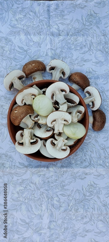 Royal mushrooms and white onions cut in half in a ceramic plate on a light tablecloth.