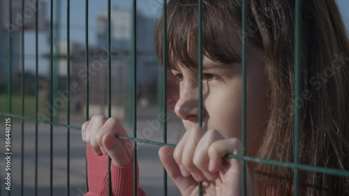 Loneliness of a teenager. A sad teenage girl behind an iron mesh looks into the distance.