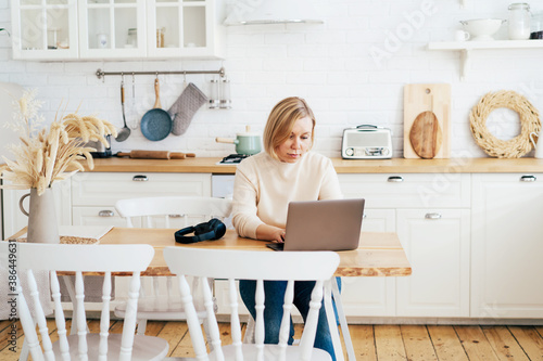 Woman working at home in kitchen wirelessly in laptop.