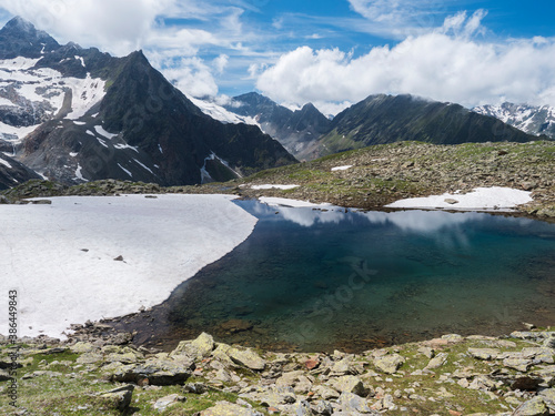 Beautiful glacial lake with springs from melting ice glacier with sharp snow-capped mountain peaks reflecting on water surface. Tyrol, Stubai Alps, Austria, summer sunny day