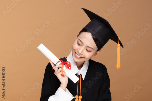Happy Graduate asian woman in cap and gowm holding Certificated or diploma on Beige background,Graduation Concept photo