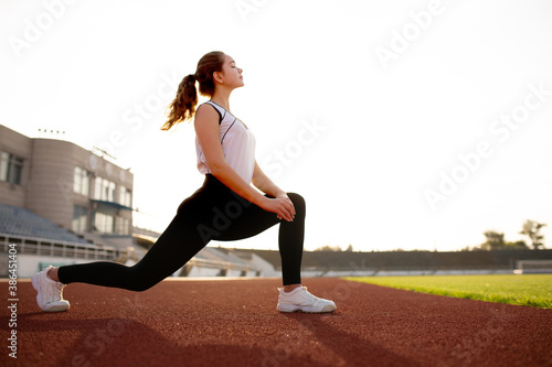 Fitness Girl Doing Workout On Yoga Mat At Outdoor Stadium. Fit Woman With Strong Muscular Body Doing back stretches Exercise Against stadium background. Active Lifestyle For Urban People