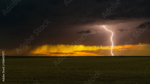 Lightning bolt streams from the sky as a vivid sunset appears behind the storm clouds