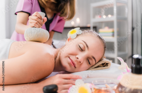 Beautiful young woman lying and relaxing with having massage by herbal compress balls in therapy spa salon. Beauty of lady in spa salon getting therapy from thai massage of asian woman in spa resort.