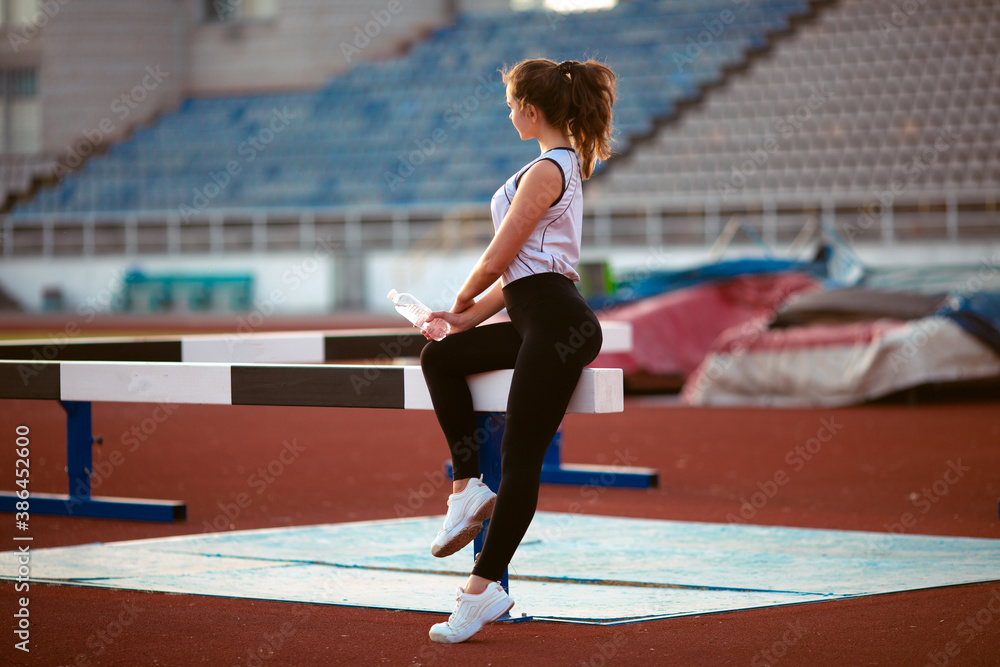 Fototapeta premium Fitness Girl Doing Workout On Yoga Mat At Outdoor Stadium. Fit Woman With Strong Muscular Body Doing back stretches Exercise Against stadium background. Active Lifestyle For Urban People