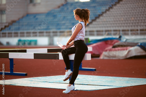 Fitness Girl Doing Workout On Yoga Mat At Outdoor Stadium. Fit Woman With Strong Muscular Body Doing back stretches Exercise Against stadium background. Active Lifestyle For Urban People