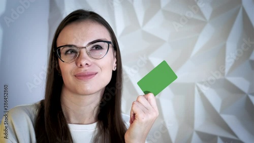 Beautiful brunette girl smiles and shows an element for advertising, with a green screen, on a white volumetric background