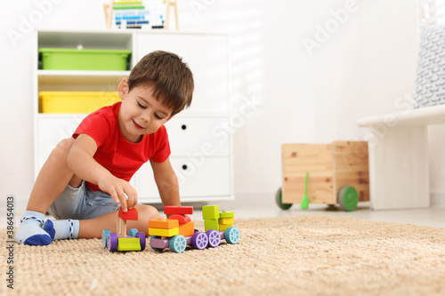 Cute little boy playing with colorful toys on floor at home, space for text