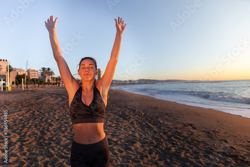 young caucasian woman doing stretches and yoga exercises on the beach on sun rising. photo