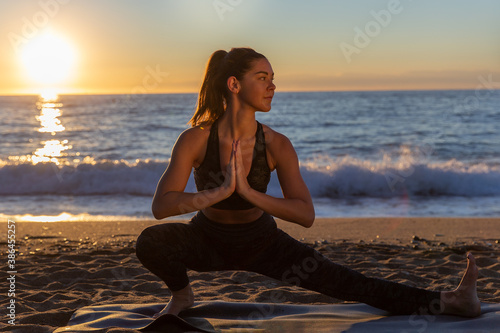 young caucasian woman doing stretches and yoga exercises on the beach on sun rising. photo