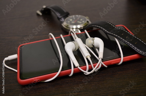 Red smartphone with white headphones and wrist watch