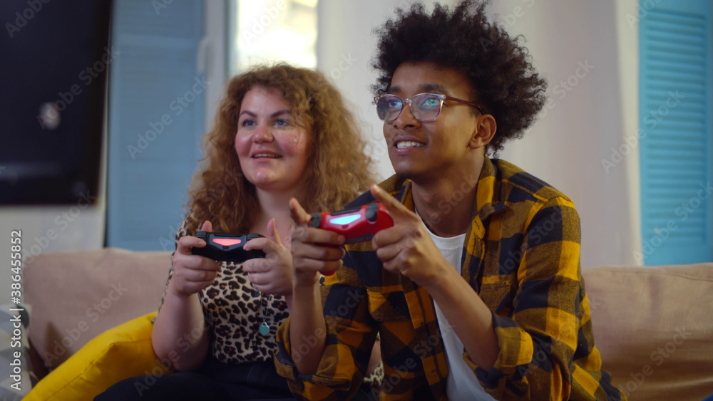 Fototapeta premium Cheerful diverse couple competing with each other in video games, holding joysticks and laughing