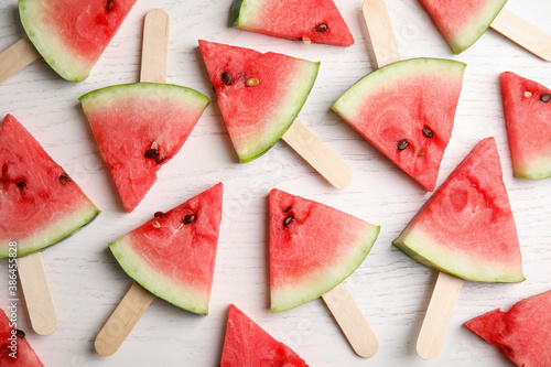 Watermelon slices with wooden sticks on white background, flat lay