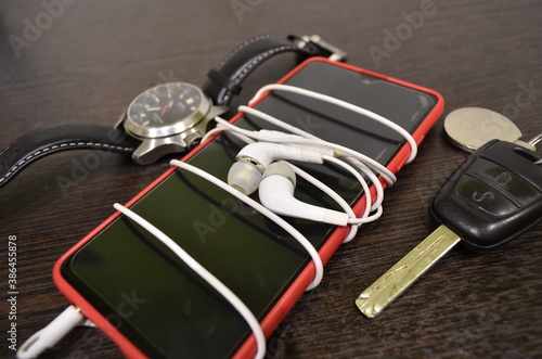 Red smartphone with white headphones, wrist watch and car key