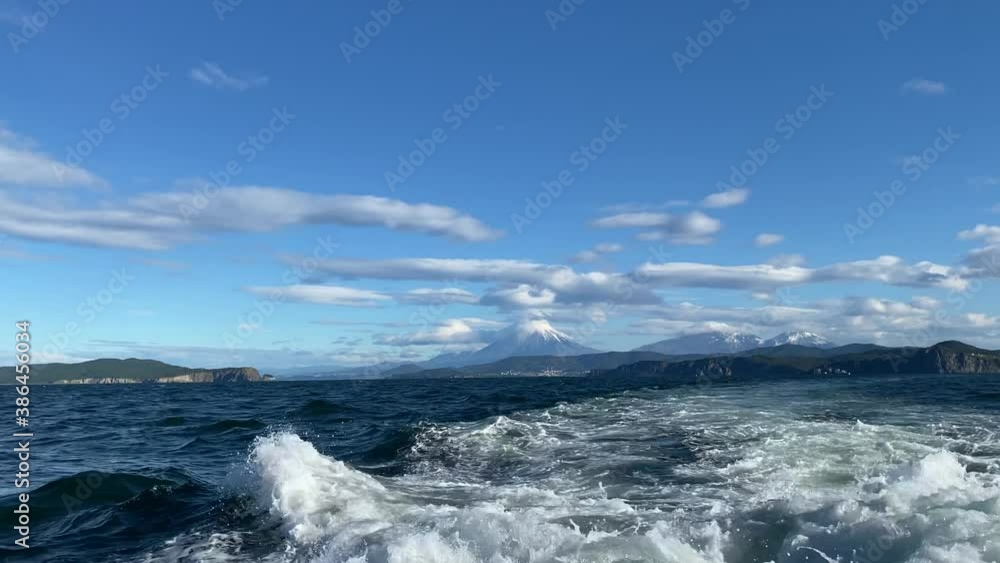 Volcanoes, mountains and hills of Kamchatka. Beautiful blue sea with waves. View from a boat to the Avachinskaya Bay of the Pacific Ocean off the southeastern coast of the Kamchatka Peninsula. Volcanoes, mountains and hills of Kamchatka. Beautiful blue sea with waves. View from a boat to the Avachinskaya Bay of the Pacific Ocean off the southeastern coast of the Kamchatka Peninsula.