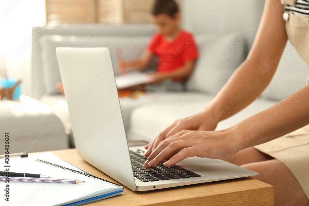 Young woman working on laptop while son drawing in living room, closeup. Home office concept Young woman working on laptop while son drawing in living room, closeup. Home office concept