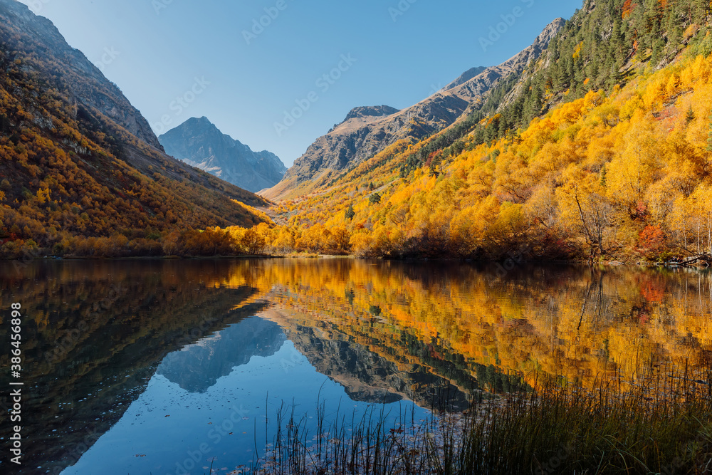 Mountain lake with transparent water and colorful autumnal trees. Mountains and scenic lake