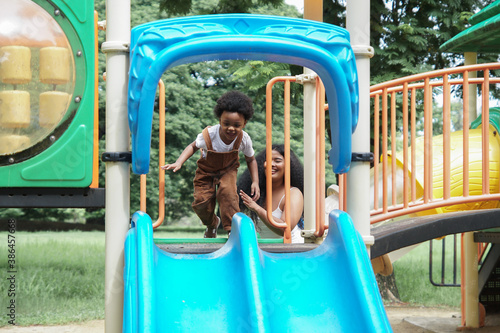 Active African little boy afro hair enjoy playing outdoors, Happy 3 Years kid having fun together with young mother on colorful slide playground in the park on a sunny day