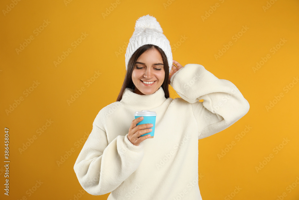 Happy beautiful woman with paper cup of mulled wine on yellow background