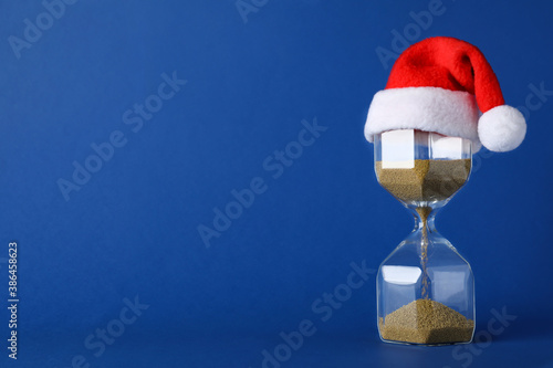 Hourglass and Santa hat on blue background, space for text. Christmas countdown