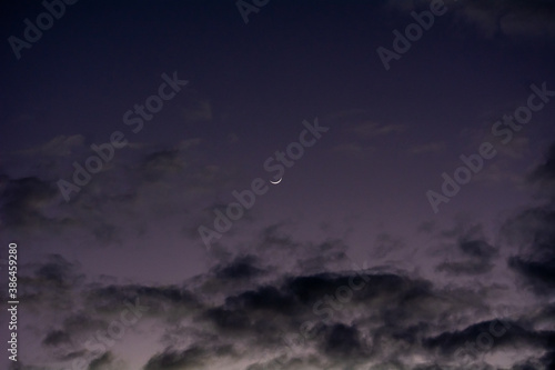 crescent moon in the sky with clouds in a dark sunset