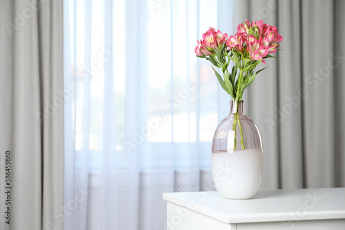 Vase with beautiful alstroemeria flowers on table near window indoors, space for text. Stylish element of interior design