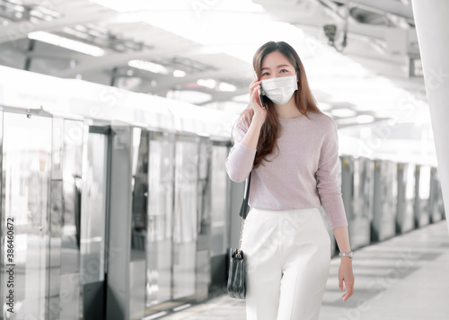 Woman wearing face mask and talking on mobile phone while standing on railway station