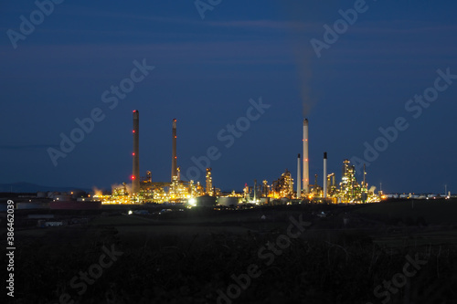 Pembroke oil refinery lit up at night with smoke rising from a chimney stack, Rhoscrowther on the Pembrokeshire coast, near Milford Haven, Wales, UK