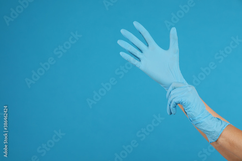 Doctor wearing medical gloves on light blue background, closeup. Space for text